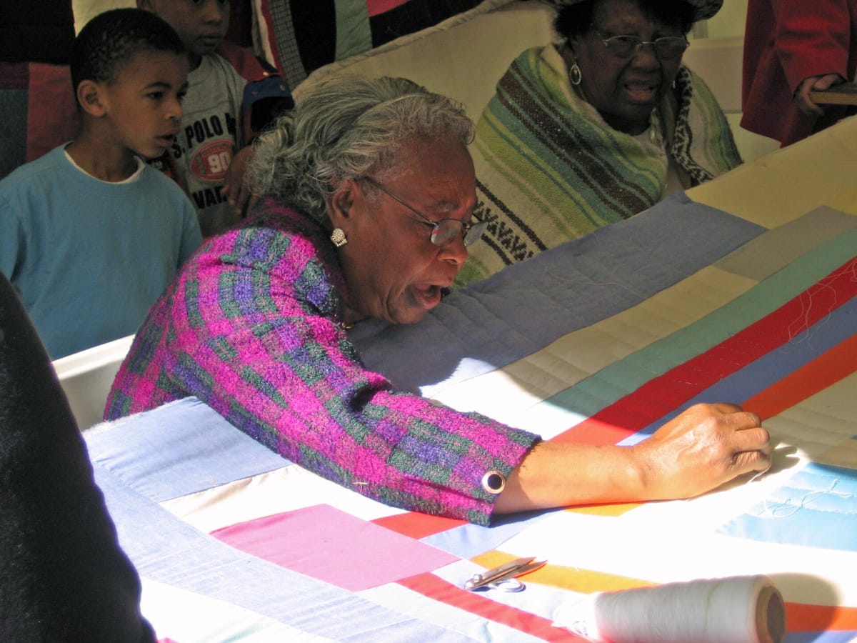 Quilter from Gee's Bend working on a quilt by hand, showing how to hand quilt