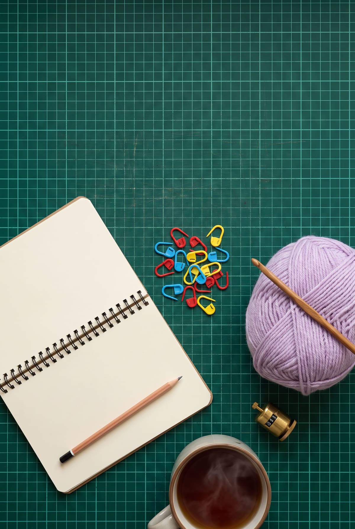 A notebook and pencil, stitch markers, lilac yarn and a crochet hook, for turning chains explained